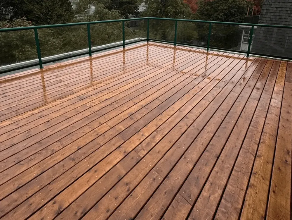 Large cedar deck with green metal railing, wet after rain, overlooking trees