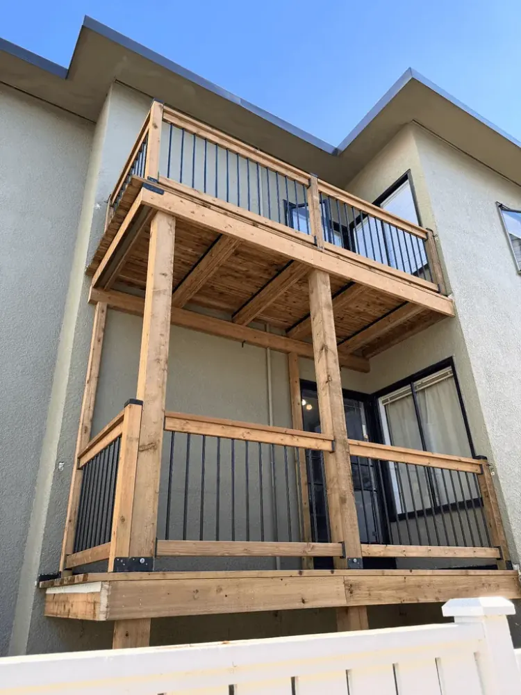 Two-storey cedar balcony with new posts, beams and black metal balusters on a stucco building